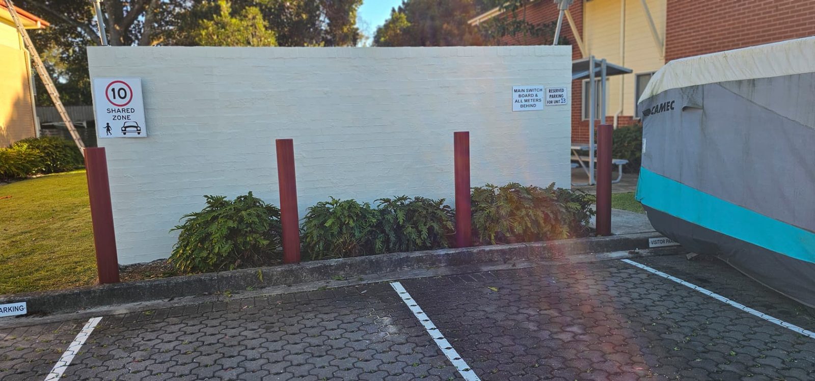 Long brick boundary wall repainted in off white beside a carpark