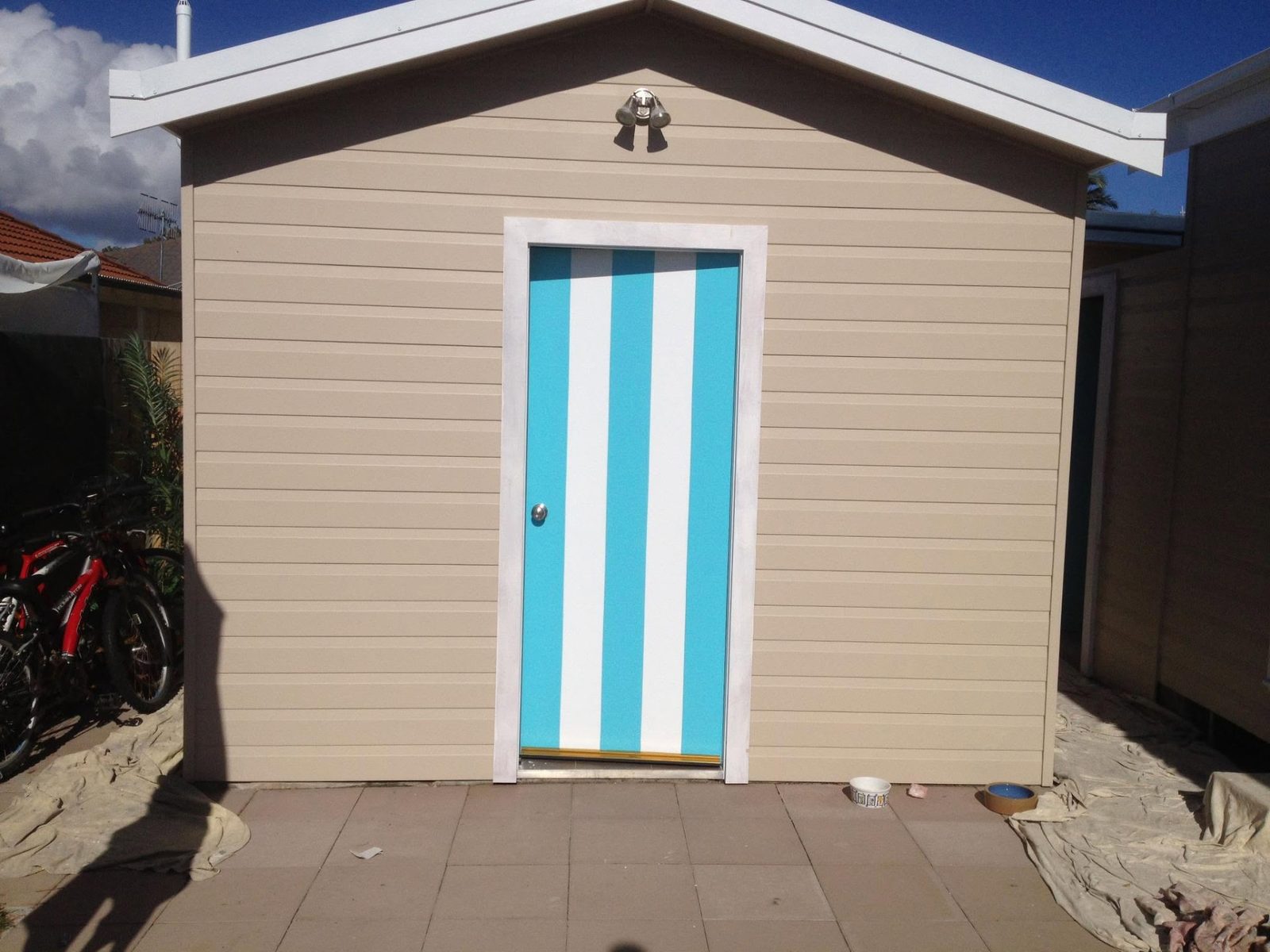 Backyard shed painted in sand with a blue and white striped door
