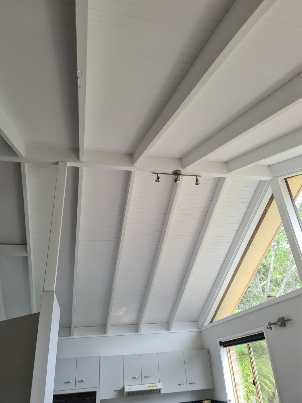 Raked white timber lined ceiling and beams above a painted kitchen