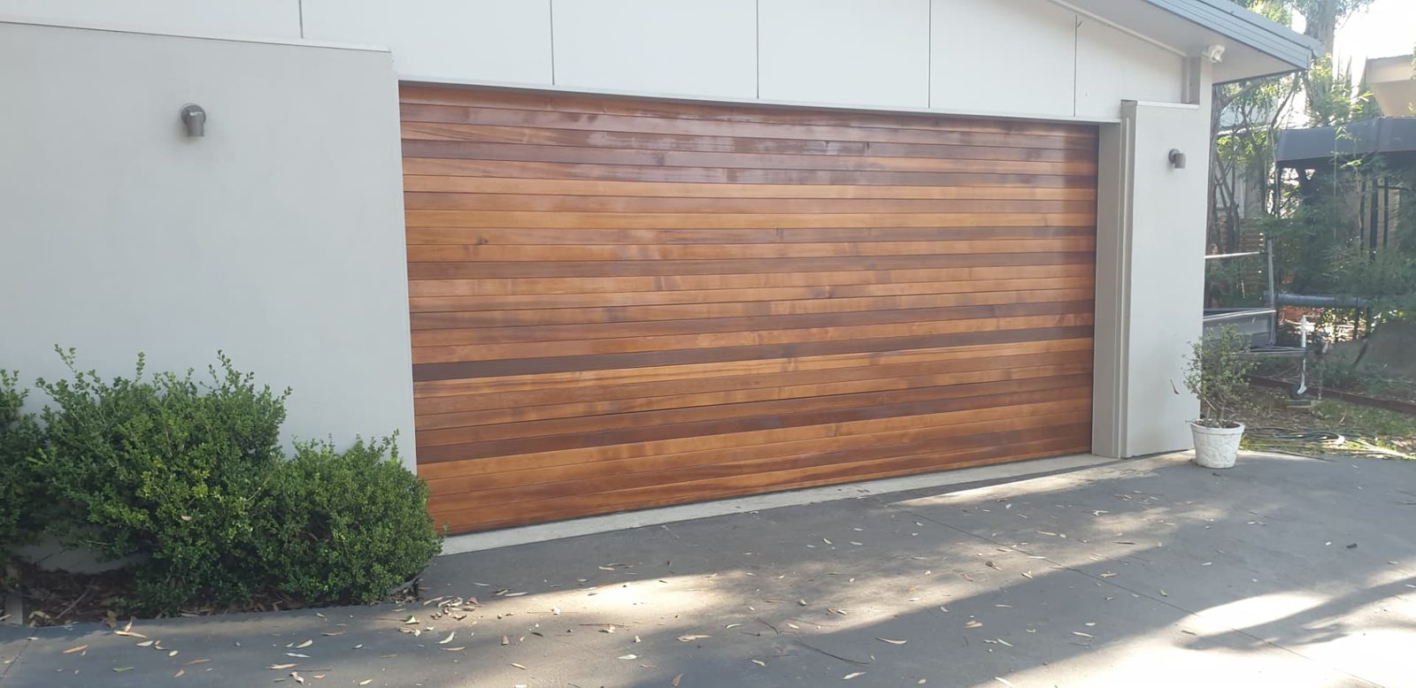 Timber garage door finished in a warm stain beside a white rendered wall